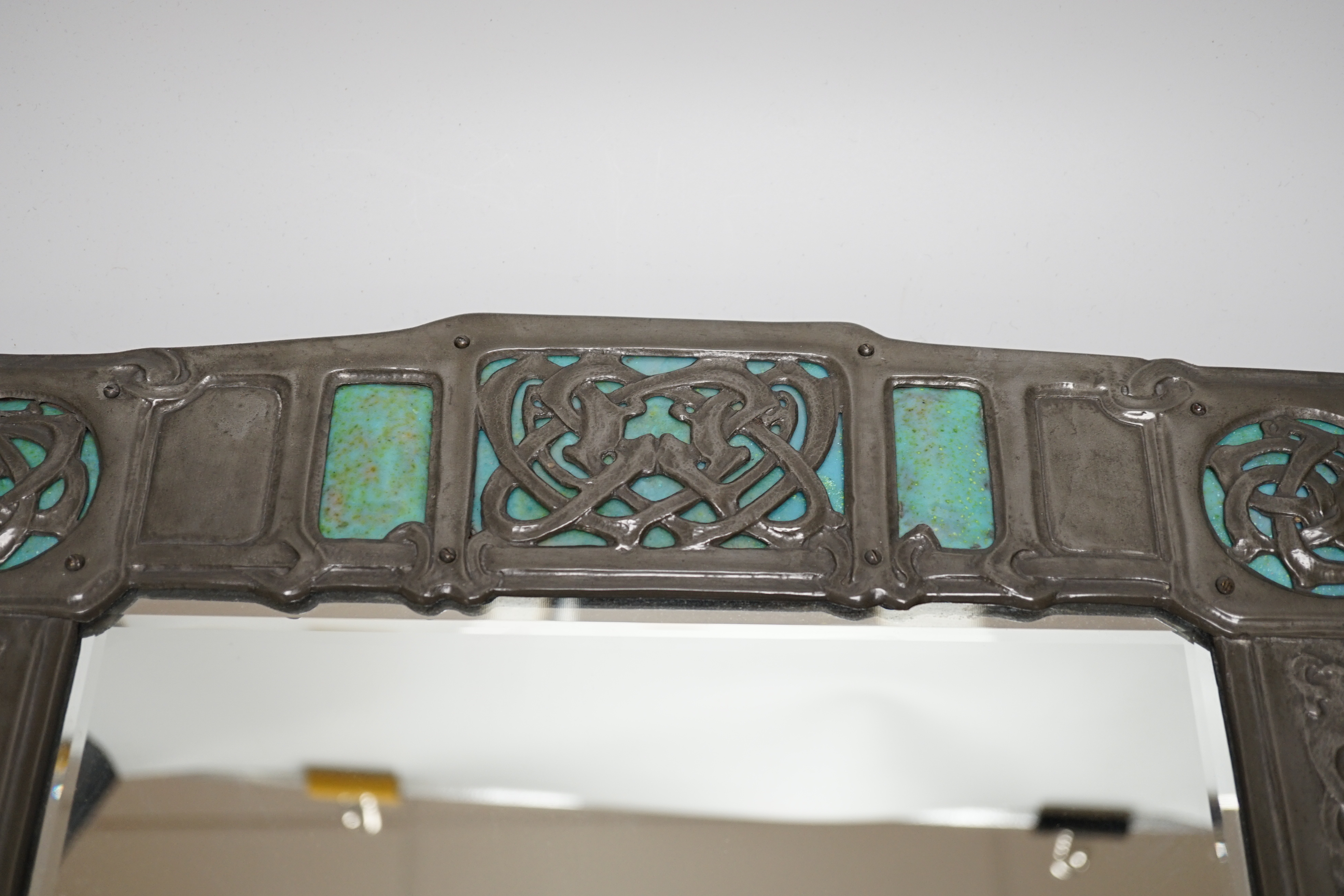 A Miller Brothers Art Nouveau embossed pewter mirror with cabochon turquoise enamel bosses, 48cm high x 39cm wide